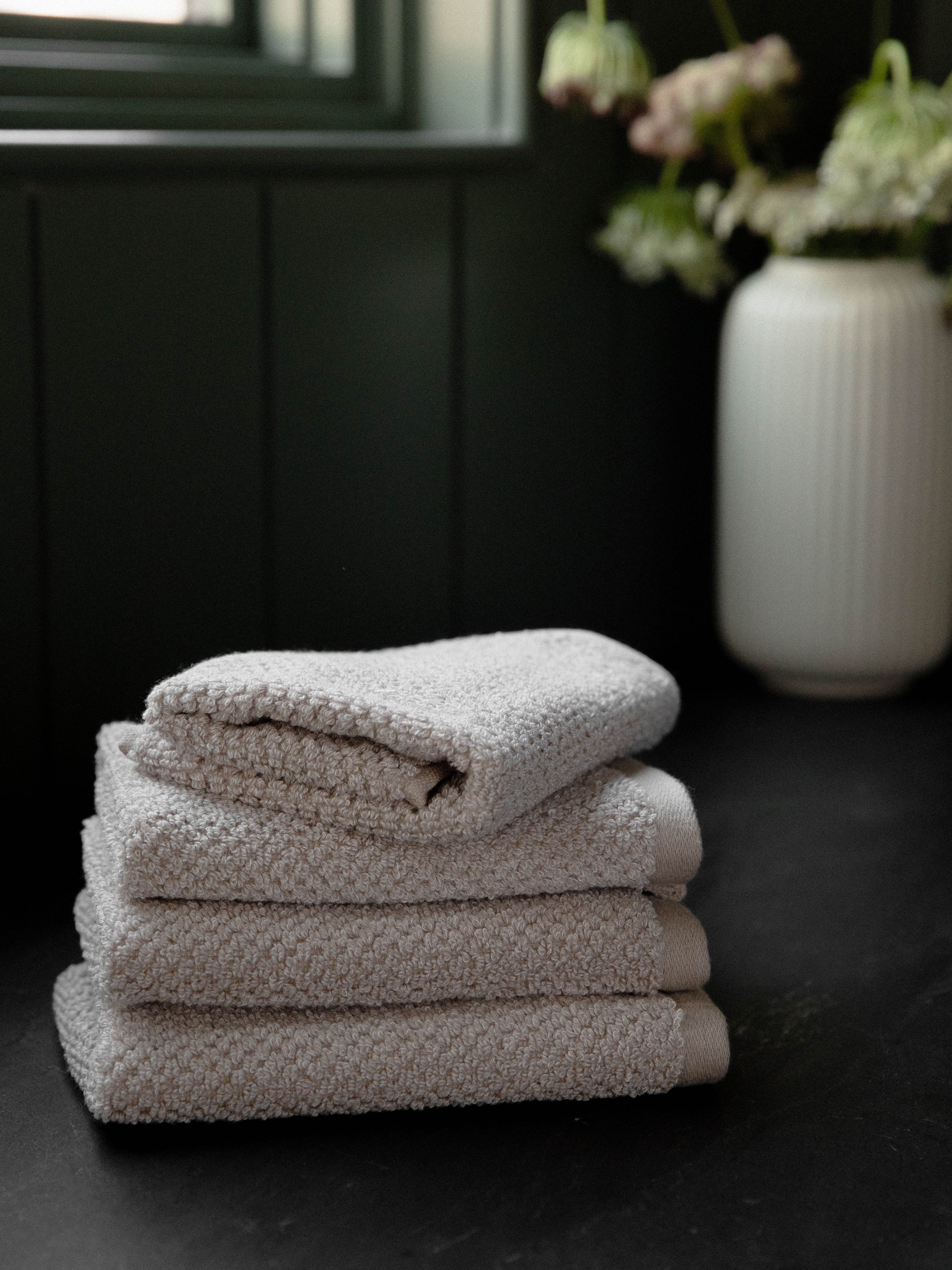Nantucket Wash Cloths in the color Heathered Sand. Photo of Nantucket Wash Cloths taken with the Wash Cloths resting on a countertop in a bathroom. |Color:Heathered Sand