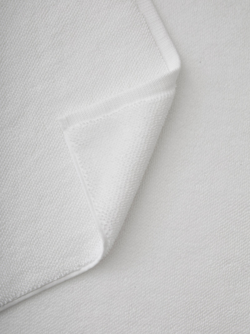 A close-up of the Cozy Earth Loop Terry Bath Mat with a folded corner highlights its soft, textured surface and neatly stitched edges, set against a background of the same material.