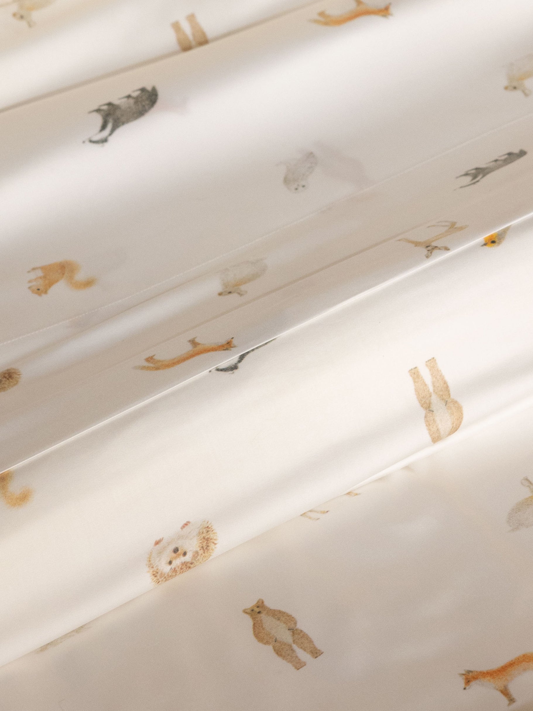 The Bamboo Fitted Sheet by Cozy Earth features a white fabric adorned with small, subtle illustrations of various animals like bears, foxes, and rabbits, evenly spaced across the surface. 
