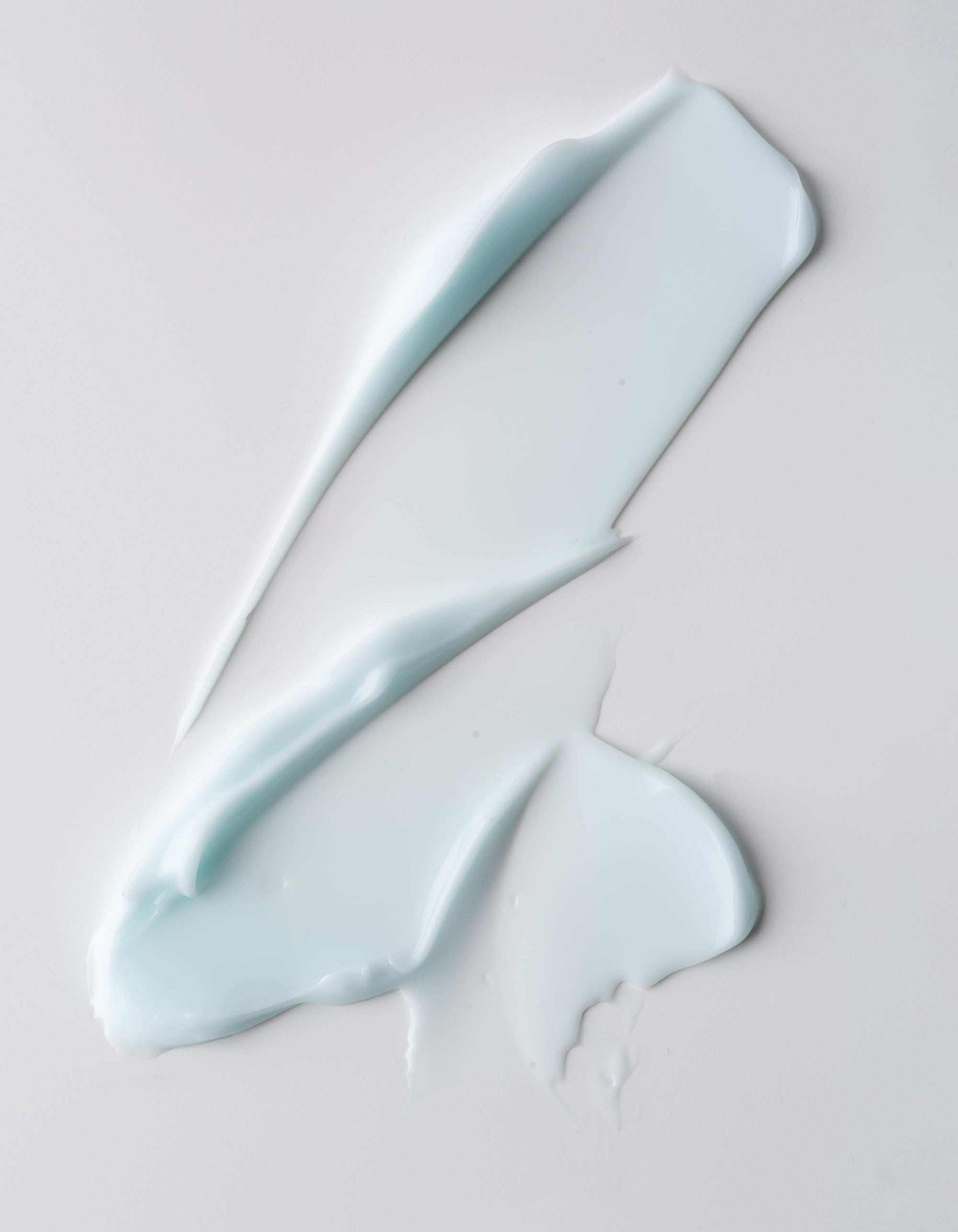 The Dewy Duo cream from Cozy Earth is a smooth, light blue product spread in swirls on a white surface. Its soft and glossy texture creates a wavy pattern with varying thickness.