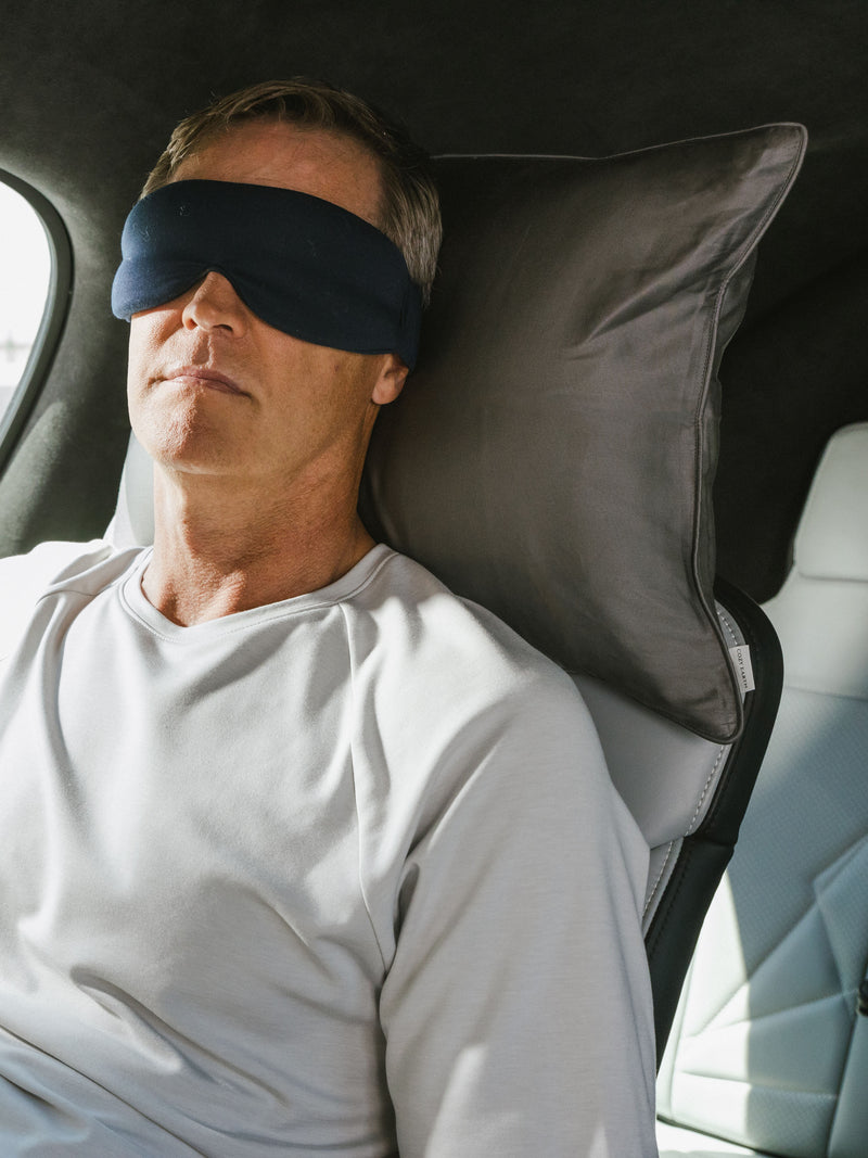 Man with sleep mask laying on travel pillow with charcoal case in the car