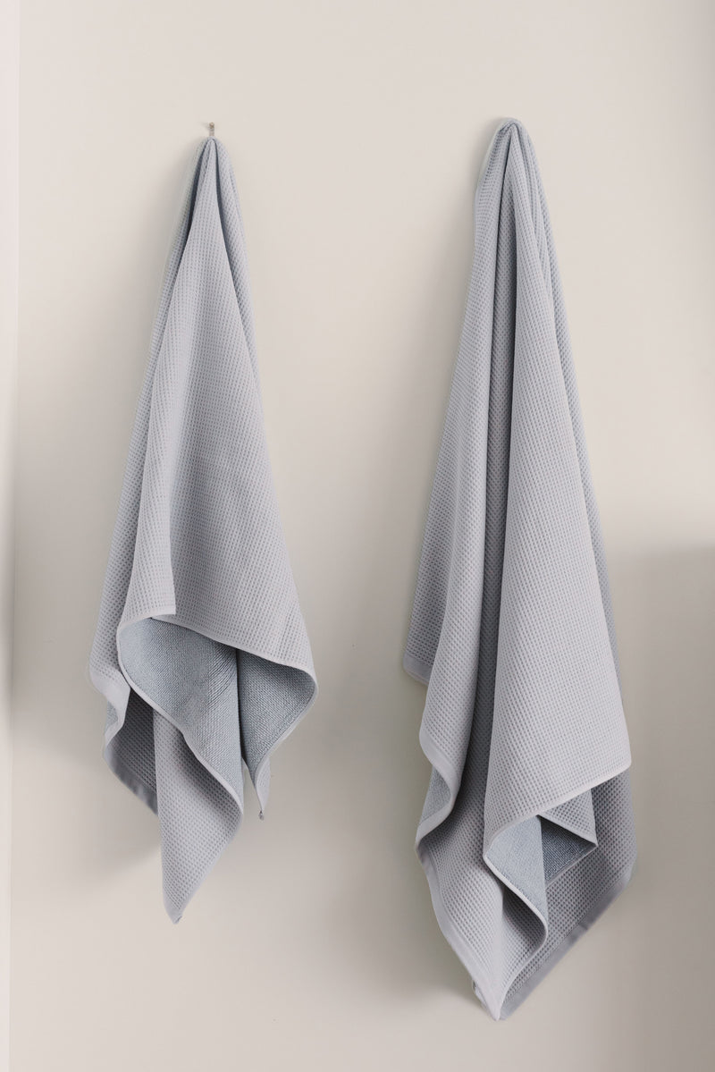 Waffle Bath Towel in the color Harbor Mist. Photo of Harbor Mist Waffle Bath Towel taken hanging from a towel hook in a white bathroom.