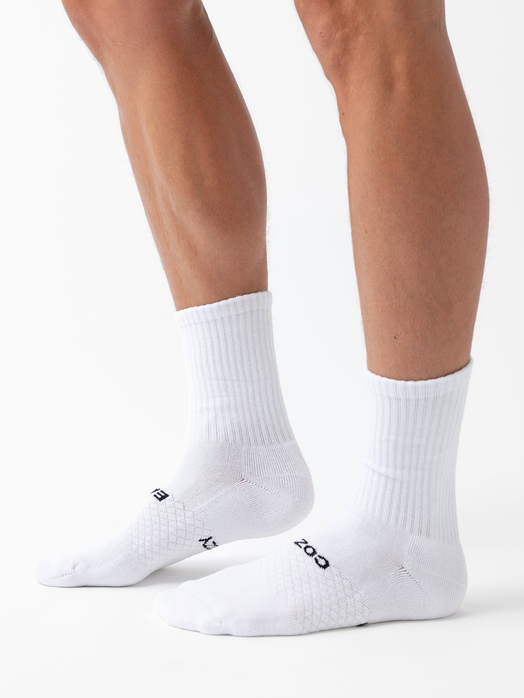 A person wears Cozy Earth Essential Calf Socks from the 8-Pack, featuring a ribbed texture and white color, with "BOSS" visible near the toes, standing on a white background. 