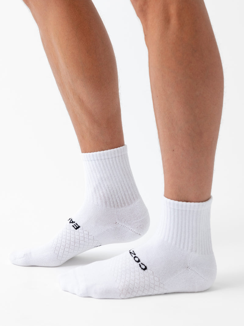 A person wears Cozy Earth's Essential Quarter Sock 8-Pack, featuring white ankle socks with ribbed cuffs and black text on top, standing against a plain white background.