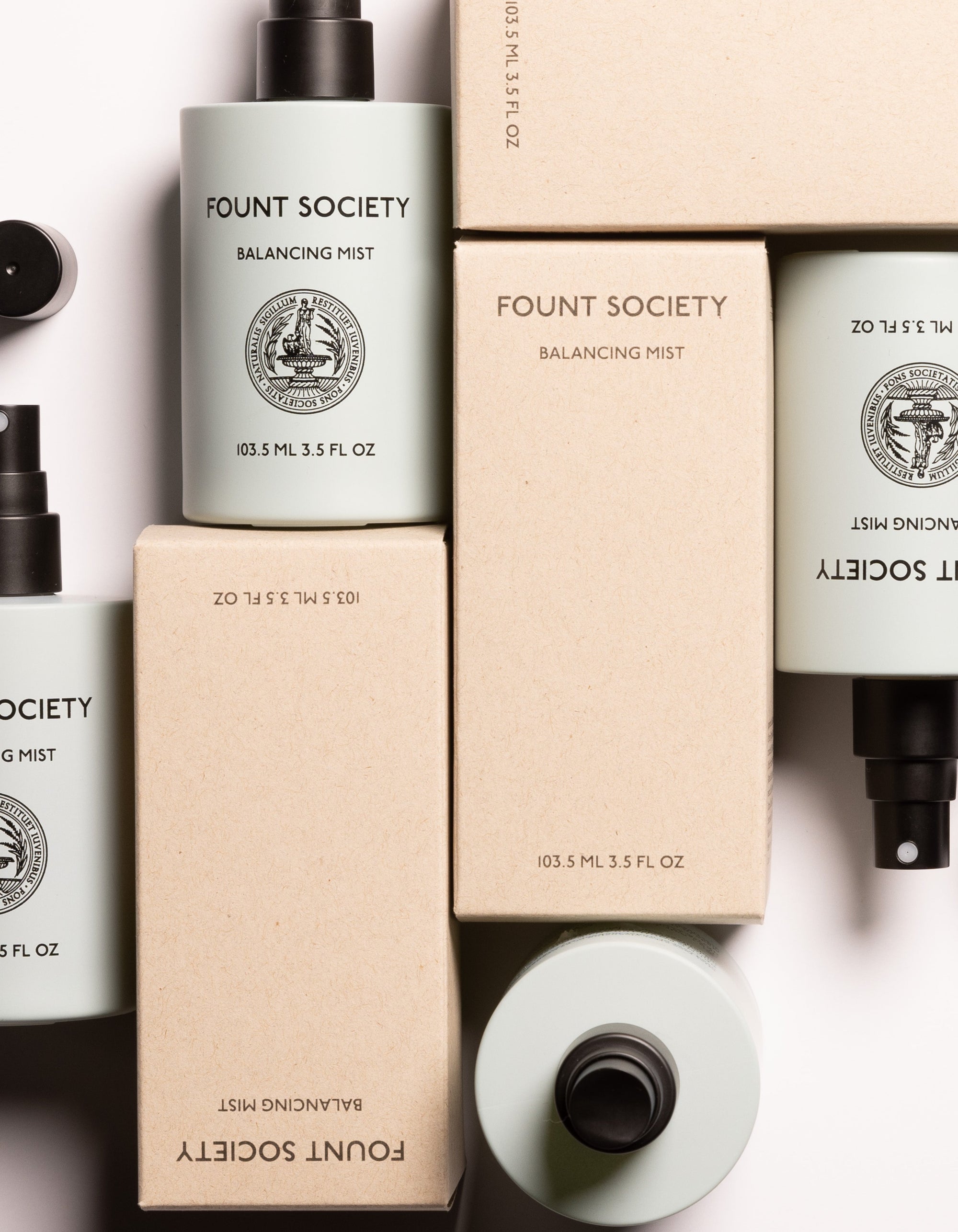 An array of Balancing Face Mist bottles by Cozy Earth, along with their packaging boxes, arranged aesthetically. The light blue-green bottles feature black spray nozzles and are labeled with the brand name "Cozy Earth," product name "Balancing Face Mist," and size (103.5 mL, 3.5 FL OZ). 