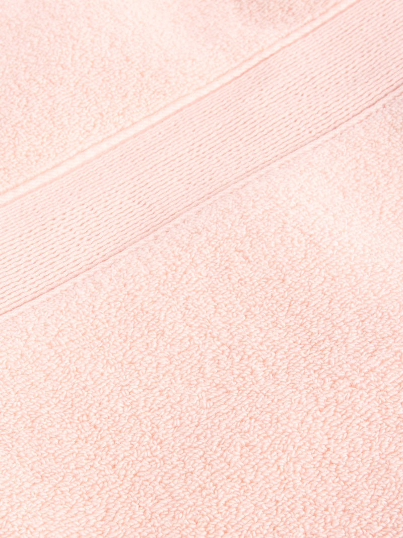 A close-up of the Luxe Hand Towel from Cozy Earth reveals its fluffy, smooth texture with a peach color and horizontal stripe pattern near the edge, suggesting comfort and absorbency.