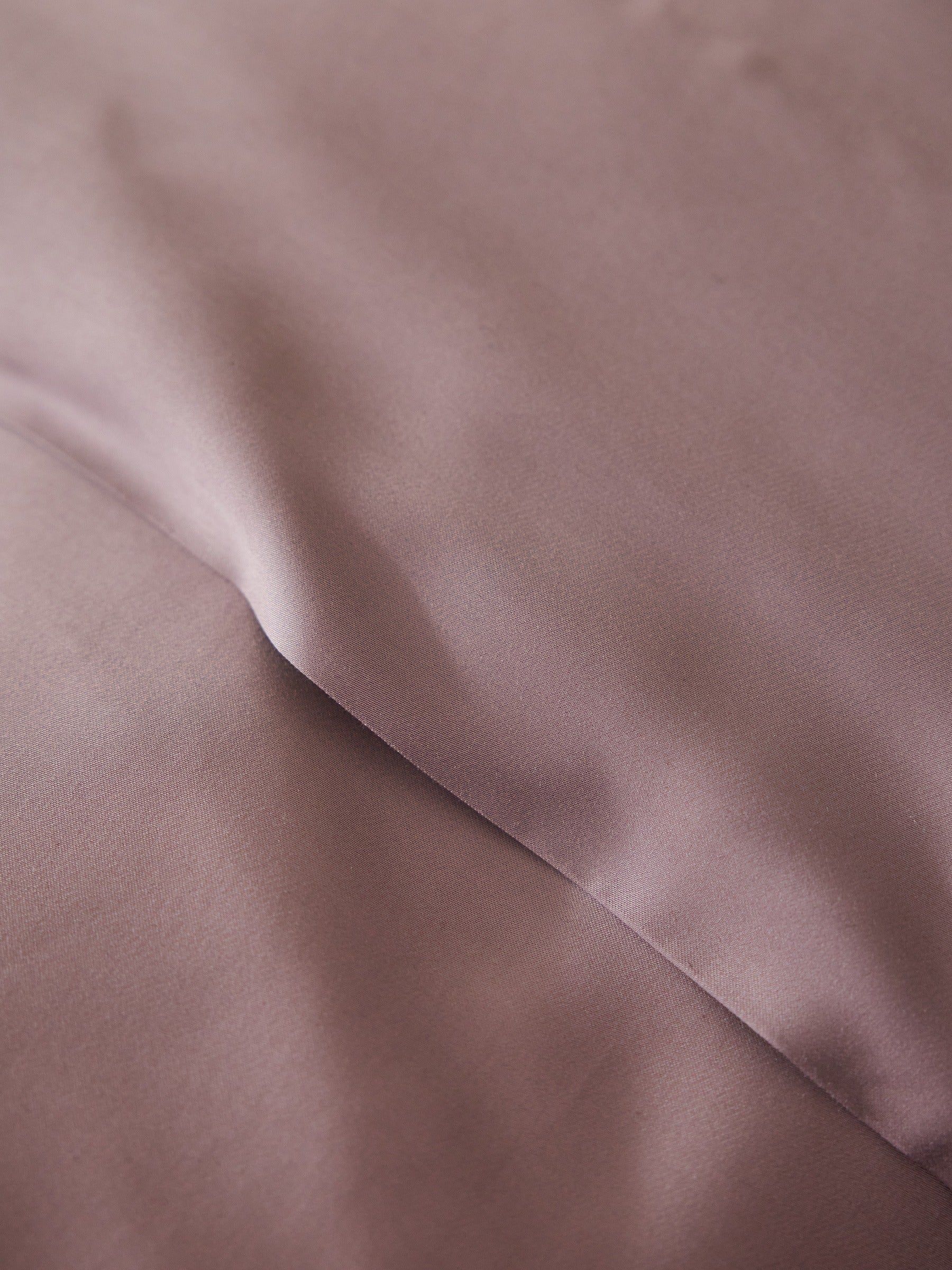 A close-up of the Bamboo Flat Sheet by Cozy Earth shows its smooth, rumpled mauve fabric with soft folds creating gentle shadows on its surface. |Color:Lavender