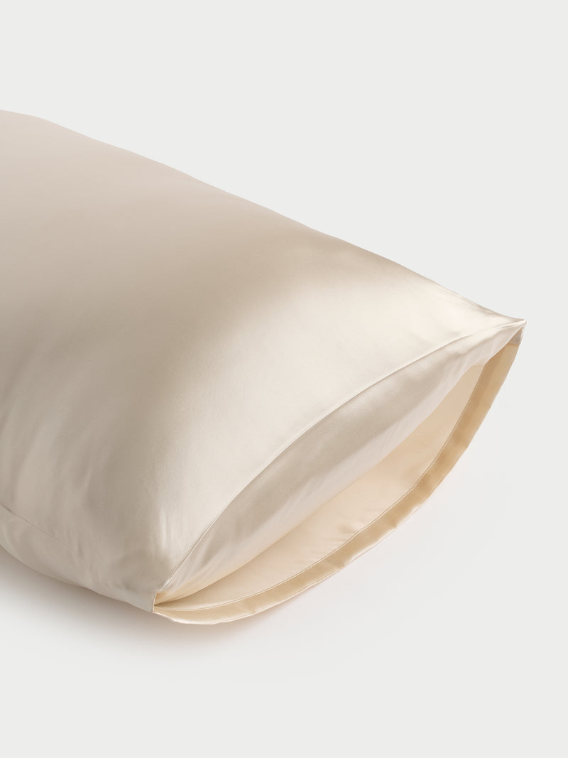 A close-up of a Cozy Earth Silk Pillowcase reveals its smooth, cream-colored surface and glossy texture against a light backdrop. The pillowcase is slightly open at one end, displaying its soft and luxurious fabric.