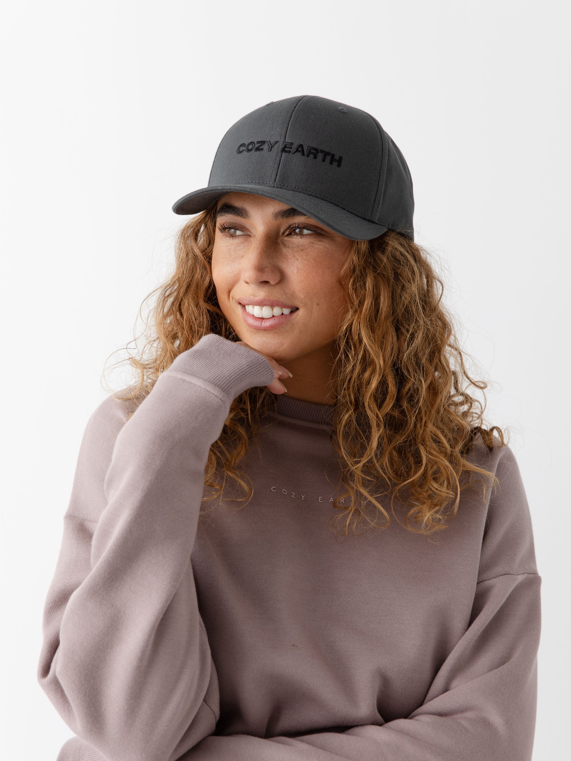 A woman wearing a grey cap with 'COZY EARTH' text on a white background 
