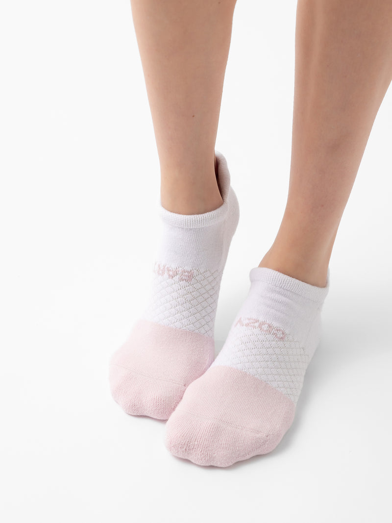 Close-up of a person's lower legs and feet wearing Cozy Earth's Essential Ankle Sock in white with a pink toe area. The socks feature a textured pattern across the top of the feet and are set against a plain white background.