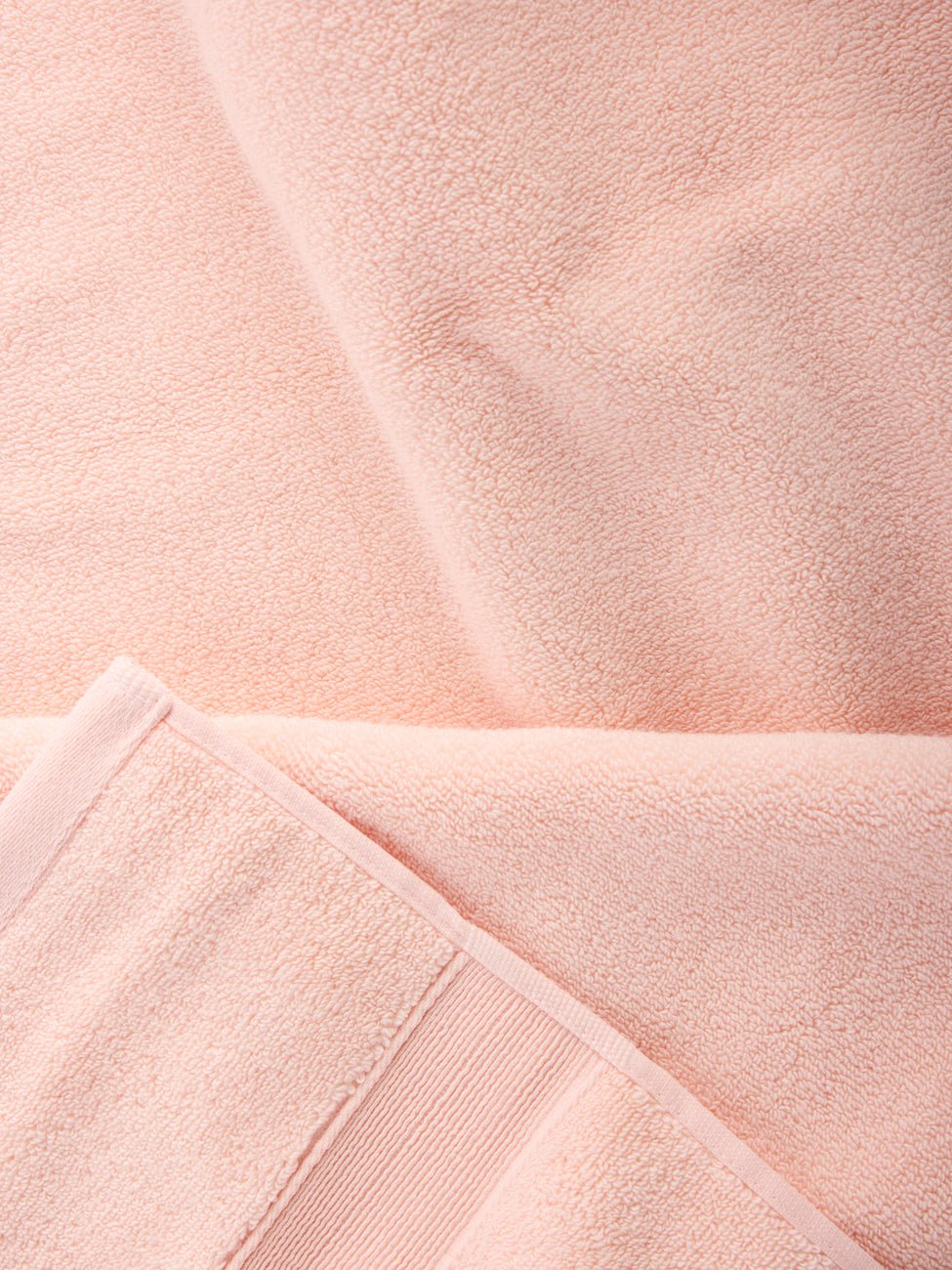 Close-up of Luxe Bath Sheets in a soft, light pink by Cozy Earth. The fabric looks plush and thick with visible texture and stitching at the edges, capturing a sense of coziness and comfort. |Color:Blossom