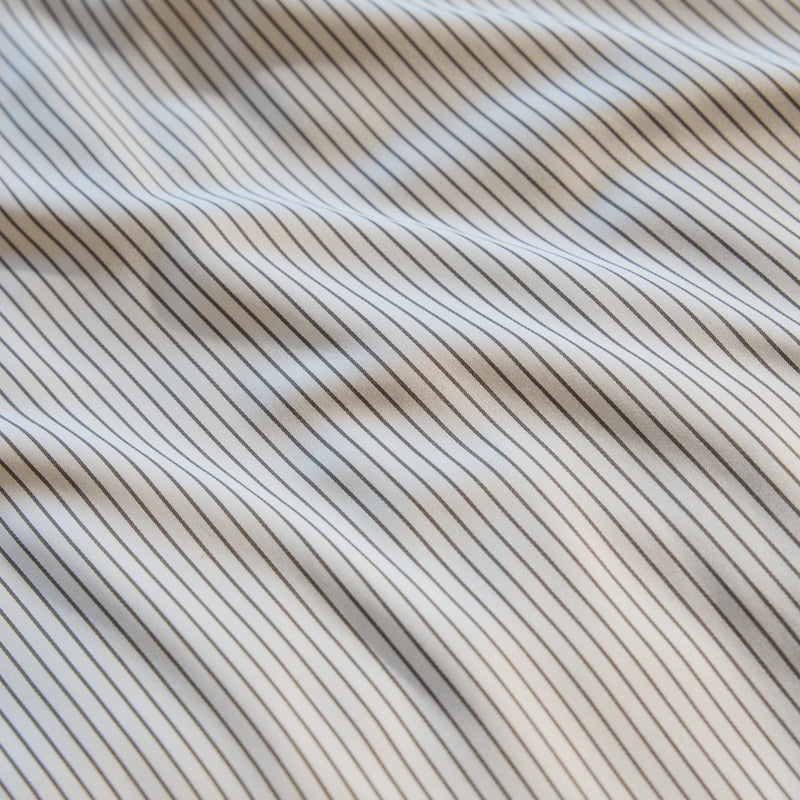 Close-up of the Bamboo Sheet Set by Cozy Earth, featuring a white fabric with thin black vertical stripes. The slightly wavy fabric creates gentle shadows and highlights, imparting a sense of texture and movement to the image.