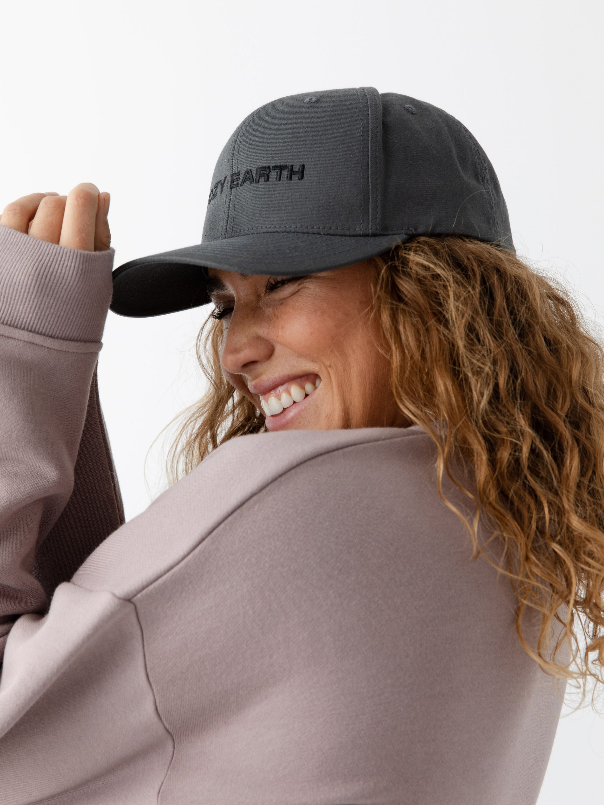 A woman wearing a grey cap with 'COZY EARTH' text on a white background 