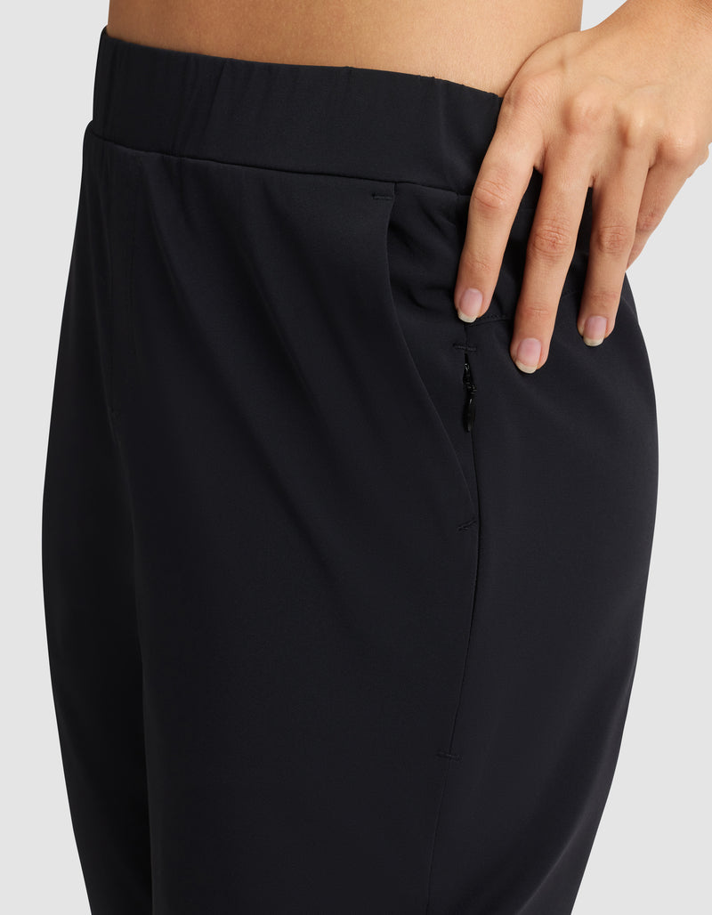 A close-up of a person wearing Cozy Earth's Women's Always Cropped Pant in black, featuring a zipper pocket and their hand resting on the waistband against a plain, light-colored background.