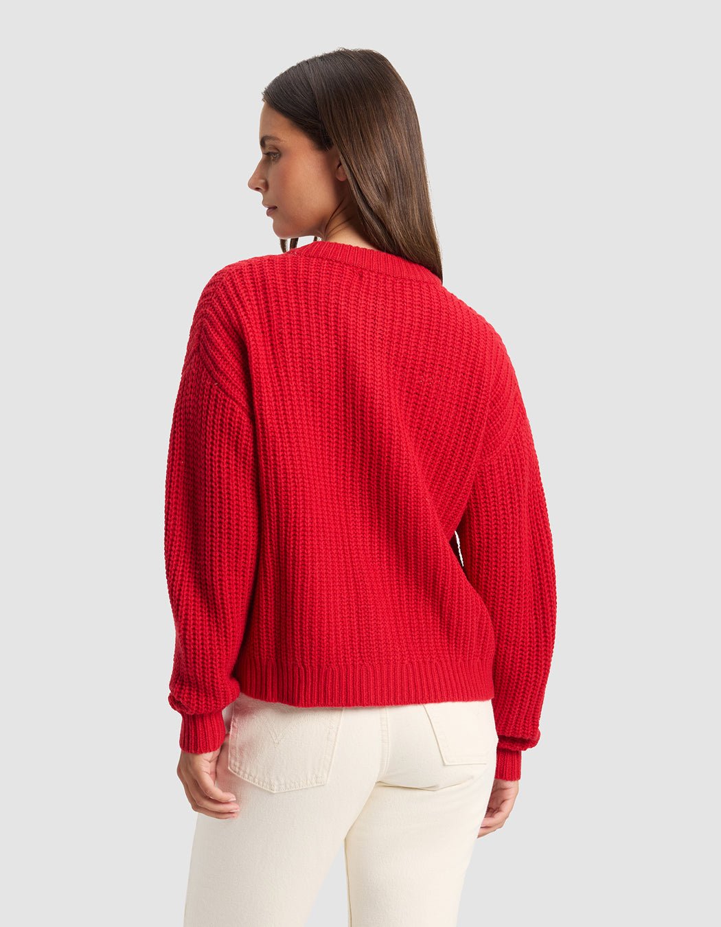 A woman with straight brown hair, seen from the back, models the Cozy Earth Women's Arden Cardigan in red and off-white pants against a plain light gray background, looking to the left.