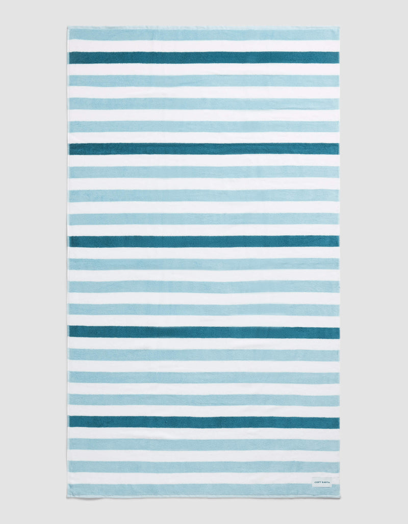 The Cozy Earth Classic Stripe Resort Towel in Lake Stripe features horizontal blue and white stripes of varying thickness and intensity, displayed flat on a neutral background.