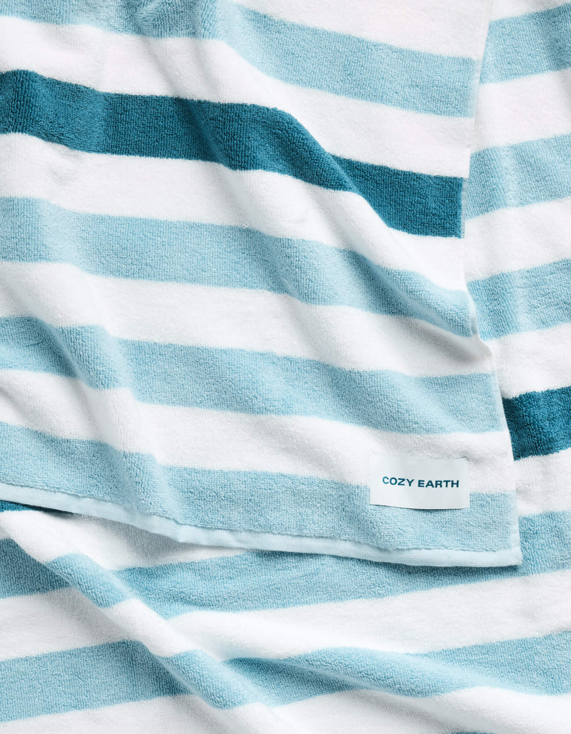 The Classic Stripe Resort Towel by Cozy Earth is a soft towel with wide blue and white horizontal stripes, featuring a small label that reads "Cozy Earth.