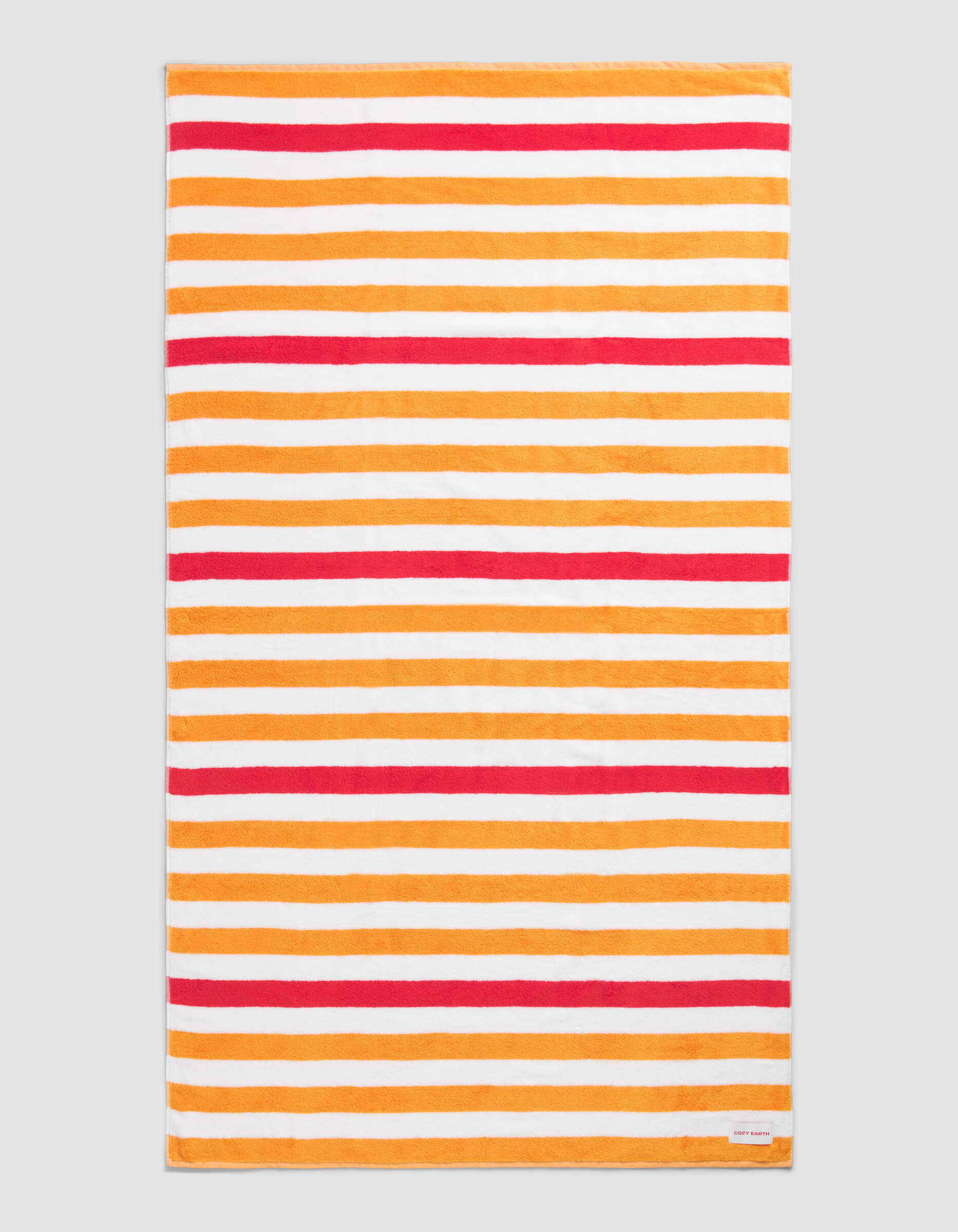 The Cozy Earth Classic Stripe Resort Towel in Mandarin Stripe features a rectangular design with horizontal orange, red, and white stripes of varying thickness on a neutral background and includes a small white corner tag.|Color:Mandarin Stripe