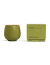 A green ceramic Candle BOTANIC by Cozy Earth sits beside its matching box, labeled with "garden basil, mint leaves, blonde woods" and "9.2 OZ | 260 G.