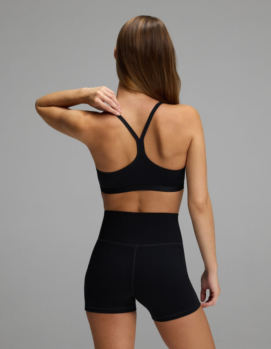 A person seen from behind, wearing a black Cozy Earth Women’s Balance Bra with racerback straps and high-waisted black shorts.|Color:Jet Black