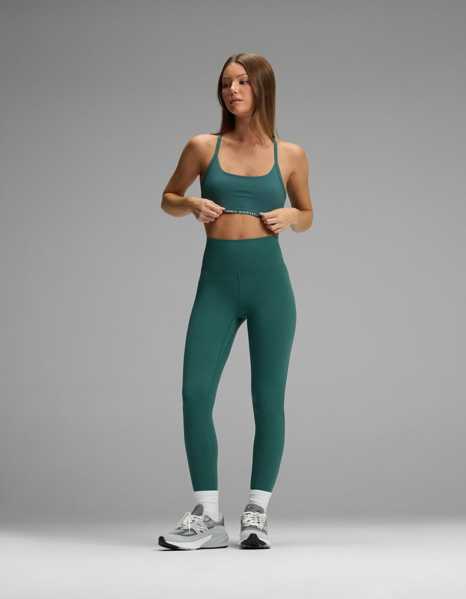 A woman wearing a dark green Cozy Earth Women’s Balance Bra and matching high-waisted leggings, white crew socks, and gray athletic shoes.