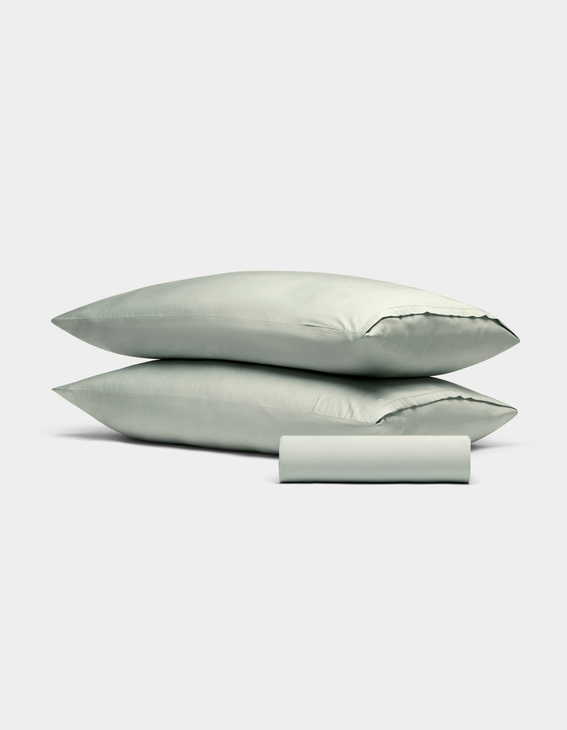 The Cozy Earth Bamboo Bedding Basic Bundle features two light gray pillows stacked together with a matching pillowcase rolled in front, all displayed against a plain white background.