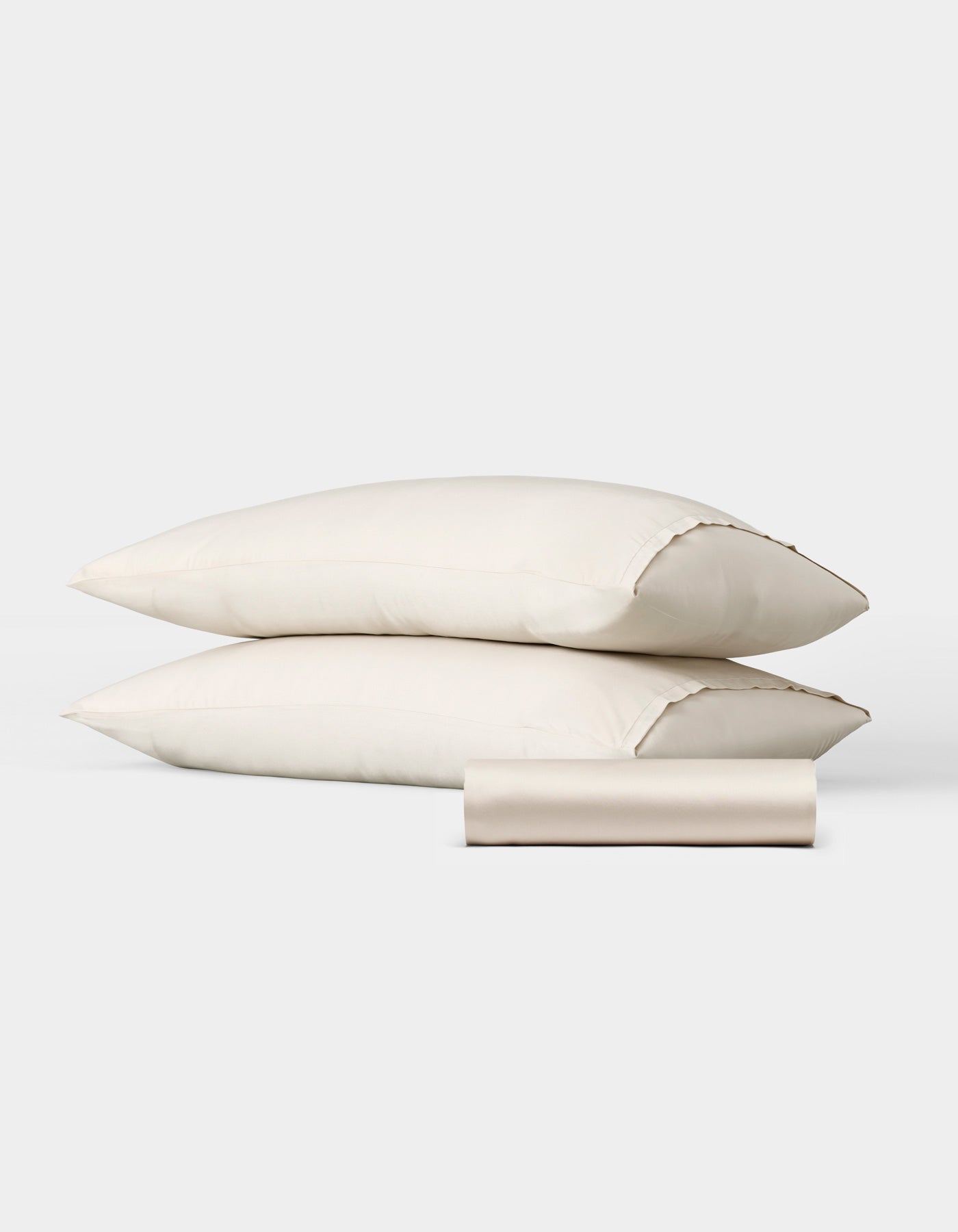 The Bamboo Bedding Basic Bundle by Cozy Earth features two cream-colored pillows stacked horizontally with a matching rolled-up fabric case in front, all displayed against a plain white background.|Color:Oat