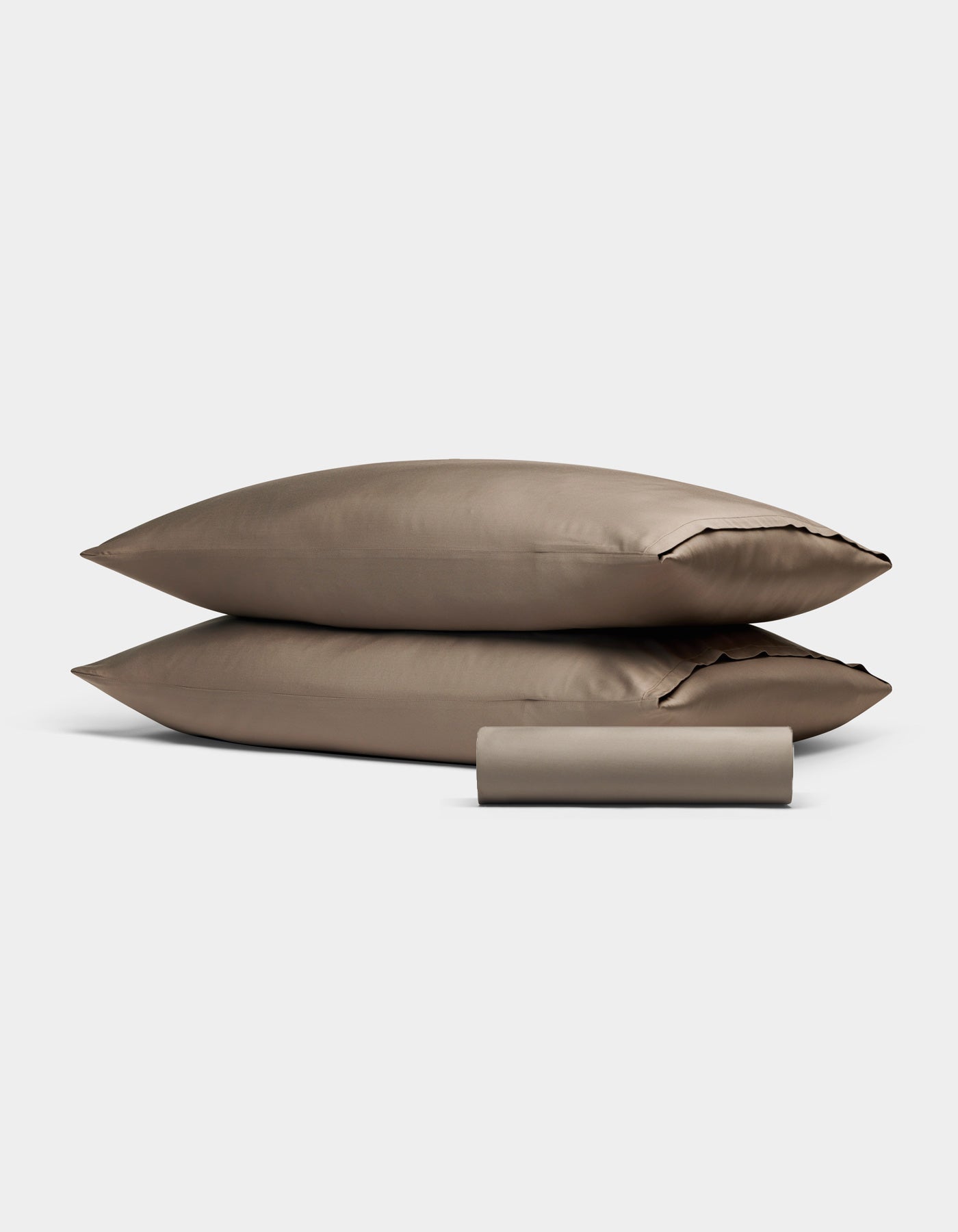 Two taupe Bamboo Bedding Basic Bundle pillowcases by Cozy Earth are stacked together, with a matching cylindrical fabric pouch in front, all set against a plain light gray background.|Color:Walnut