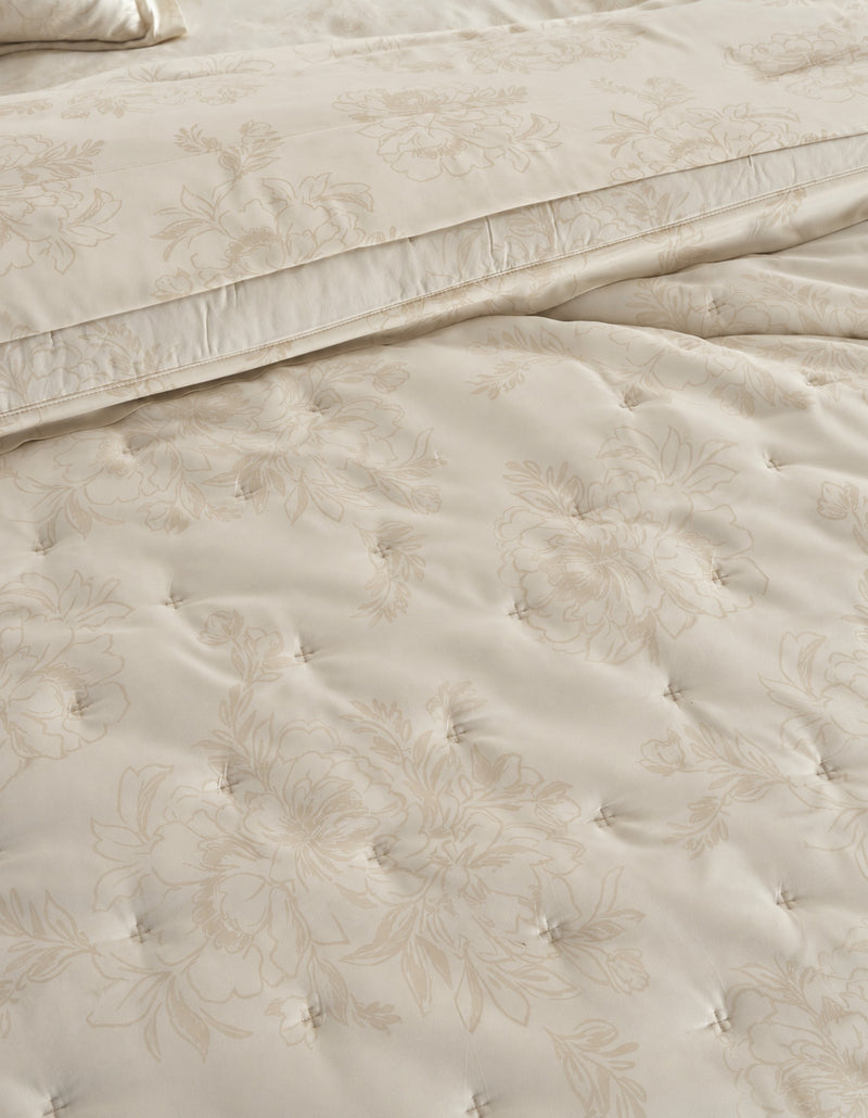 Close-up of a cream-colored quilted bedding set with a subtle floral jacquard pattern, showing the texture of the tufted comforter and matching pillowcase.