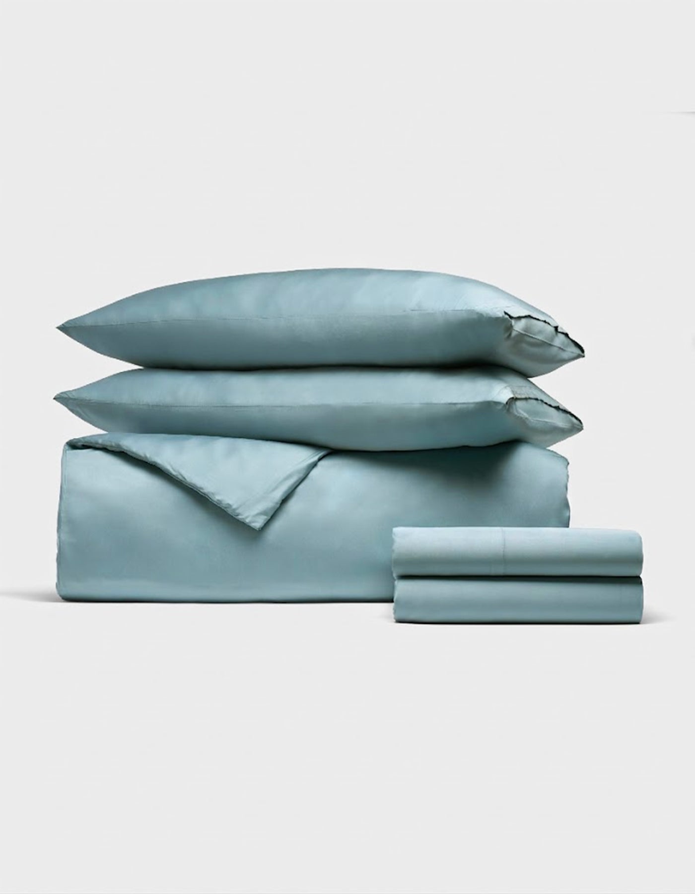 The Bamboo Bedding Deluxe Bundle by Cozy Earth features a neatly folded light blue set—including two pillows, a duvet cover, and sheets—elegantly displayed against a plain white background. 