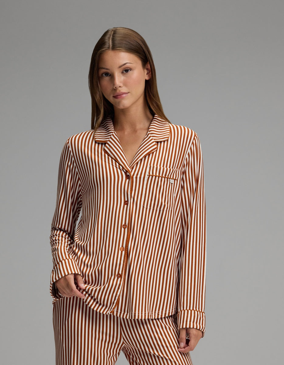 A person stands facing the camera against a plain gray background, wearing the Cozy Earth Women’s Bamboo Stretch-Knit Long Sleeve Pajama Top, featuring matching brown and white vertical stripes.|Color:Market Stripe in Cinnamon