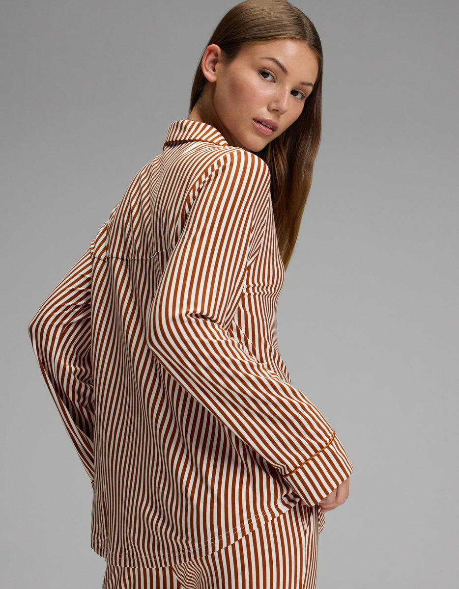 A woman with long brown hair poses sideways, looking over her shoulder against a plain gray background while wearing the Cozy Earth Women’s Bamboo Stretch-Knit Long Sleeve Pajama Top.|Color:Market Stripe in Cinnamon