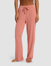 A woman is wearing Cozy Earth's Women's Bamboo Stretch-Knit Pant, featuring a loose fit and drawstring waist, standing barefoot against a plain background.|Color:Sunset Mini Stripe