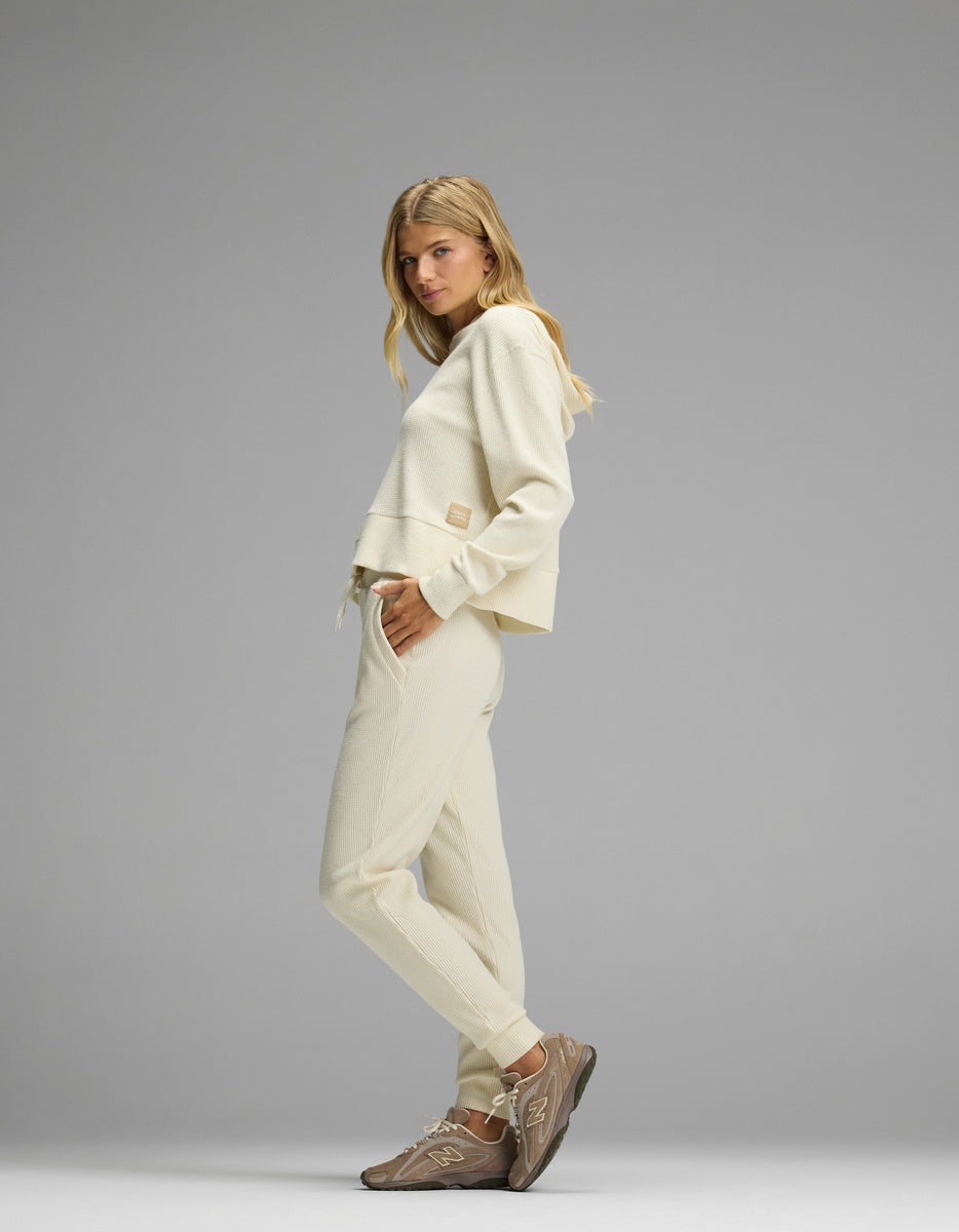 A woman models the cream-colored Women’s Blake Waffle Hoodie & Jogger Set, paired with brown sneakers.|Color:Coconut
