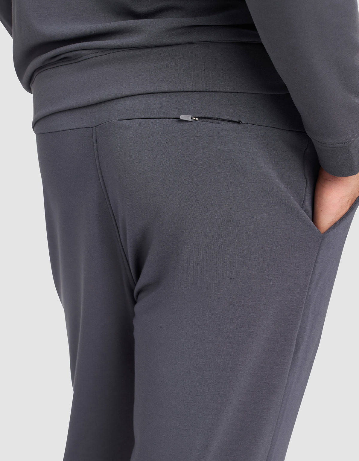 A person wearing Cozy Earth Men's Brushed Bamboo Jogger Pant in dark gray, with one hand in the pocket, showcases a close-up of the waist and upper legs plus a visible back zipper detail.