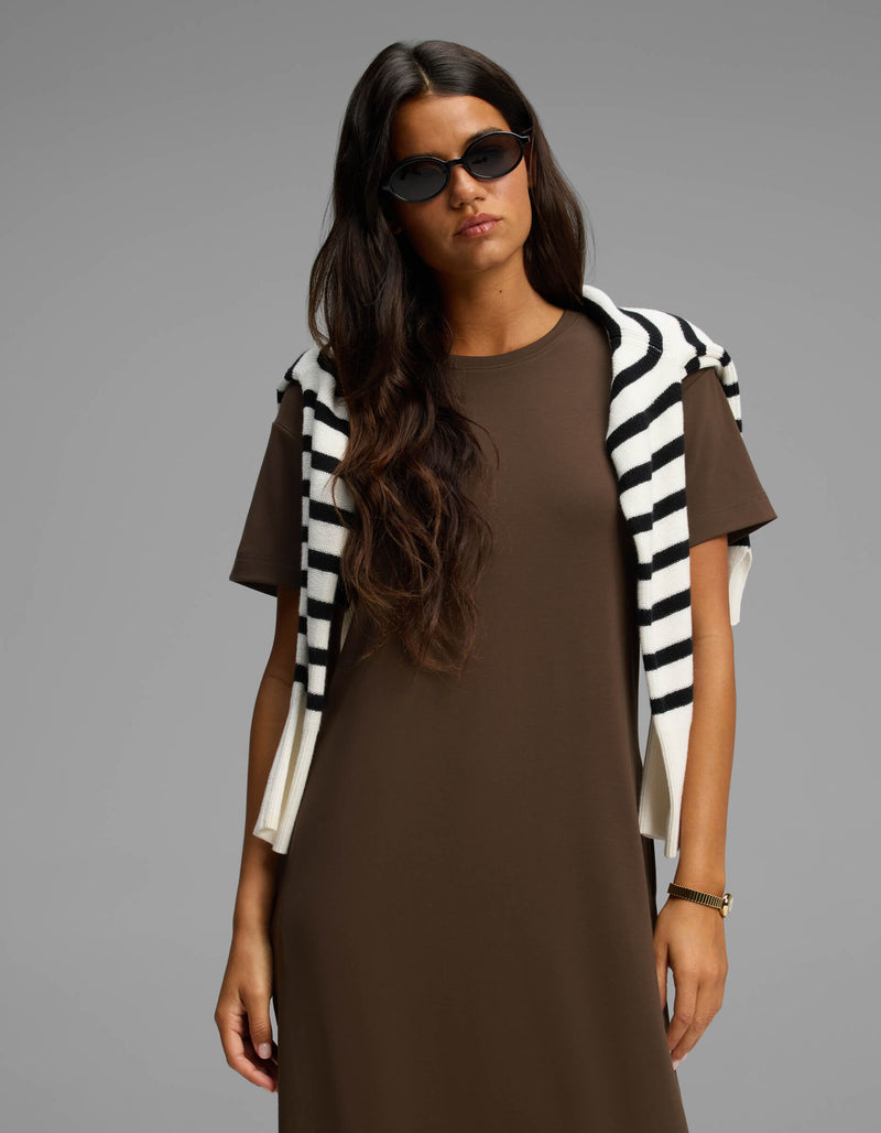 A woman with long brown hair wearing black sunglasses and a Cozy Earth Women's Brushed Bamboo Midi Dress stands against a plain gray background, with a black-and-white striped sweater draped over her shoulders.