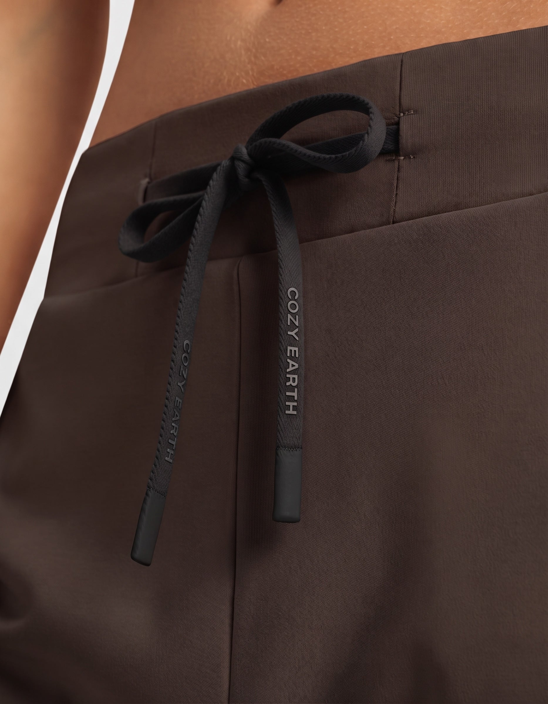 Close-up of a person wearing the Women's Brushed Bamboo Jogger Set by Cozy Earth, featuring brown pants with a black drawstring tied in a bow and "COZY EARTH" printed in white lettering.