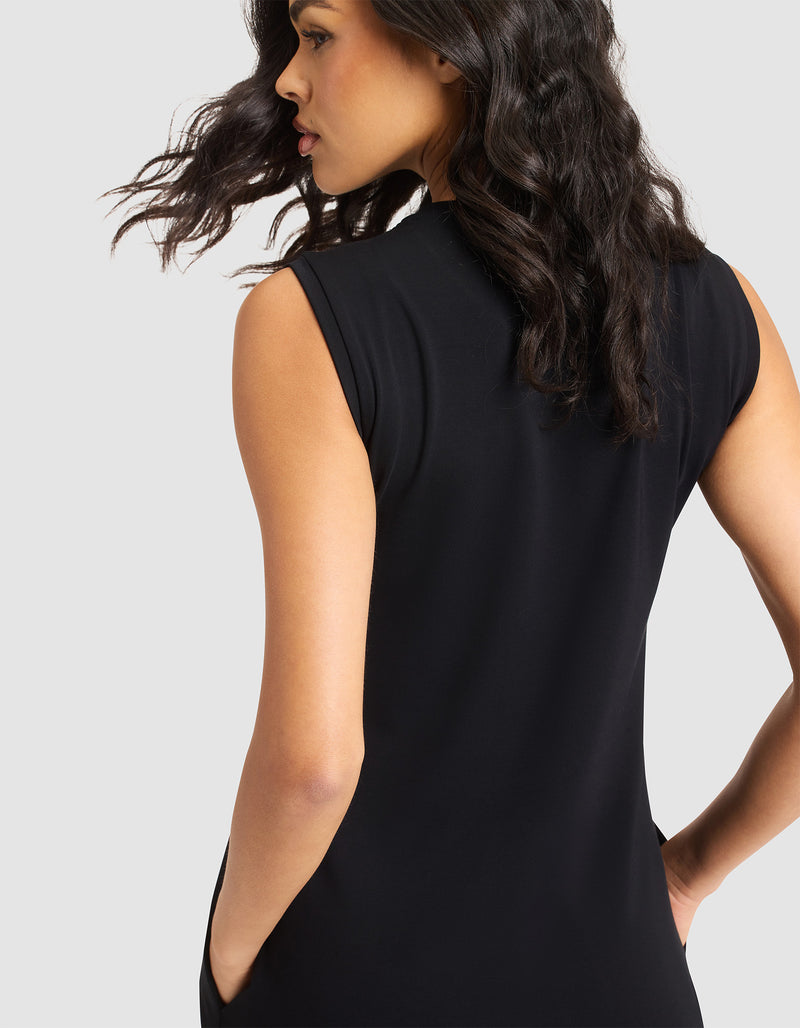 A woman with wavy dark hair models the Cozy Earth Women's Brushed Bamboo Sleeveless Midi Dress in black, standing against a light background with her back mostly to the camera and her head turned slightly to the side.