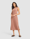 A woman models the Cozy Earth Women's Brushed Bamboo Sleeveless Midi Dress in light brown, paired with black slide sandals featuring gold accents, posing against a plain light gray background. |Color:Saddle
