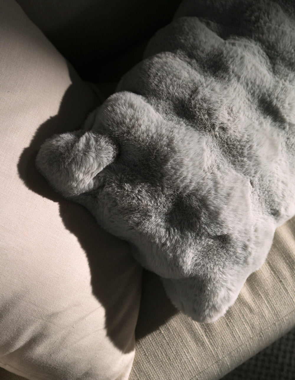 A Cozy Earth Bubble Cuddle Pillow rests on a beige fabric couch, its plush texture highlighted by gentle sunlight that casts soft shadows across the inviting scene.