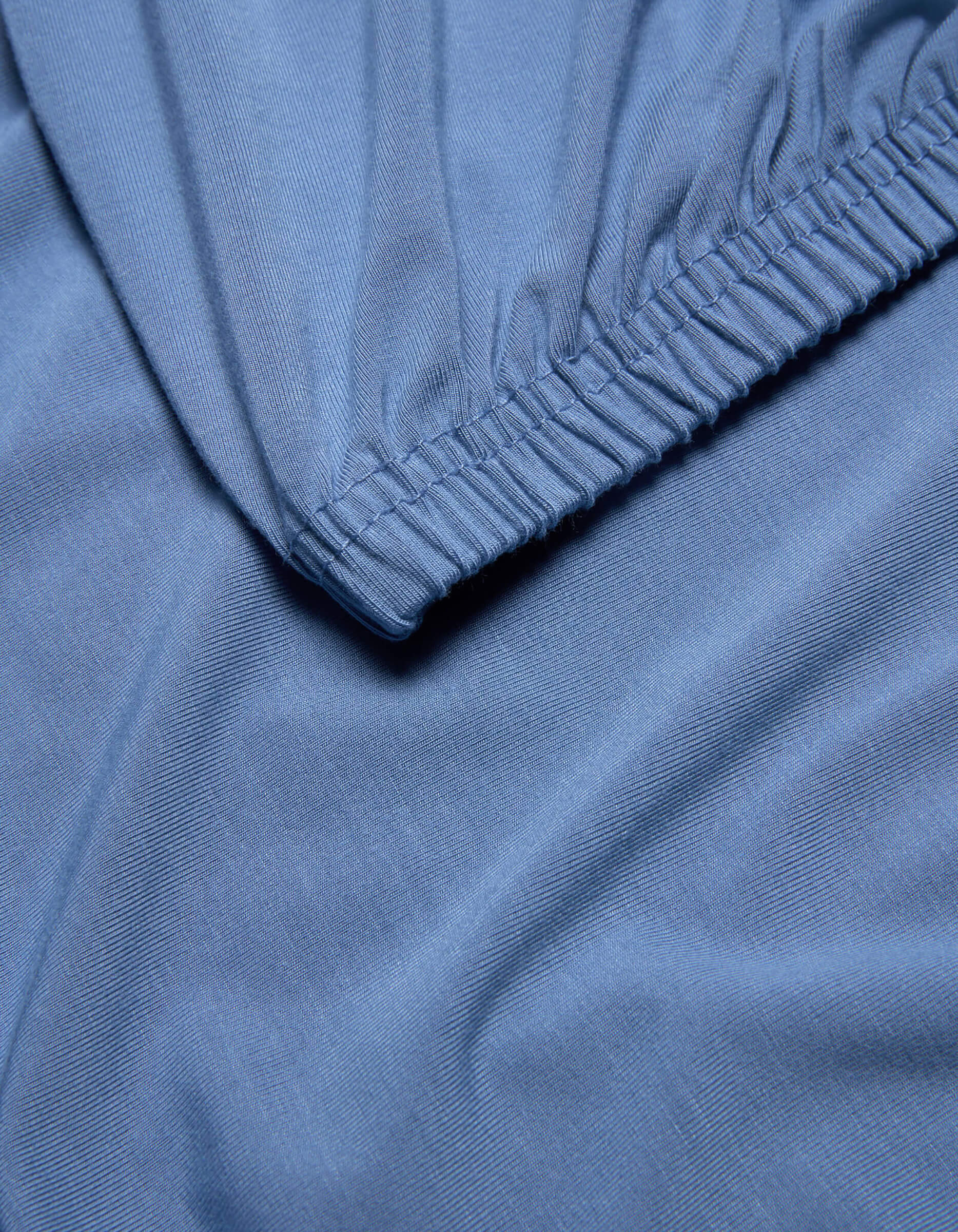 Close-up of light blue Bamboo Jersey Fitted Sheet by Cozy Earth, featuring an elastic edge, smooth texture, and gentle folds.