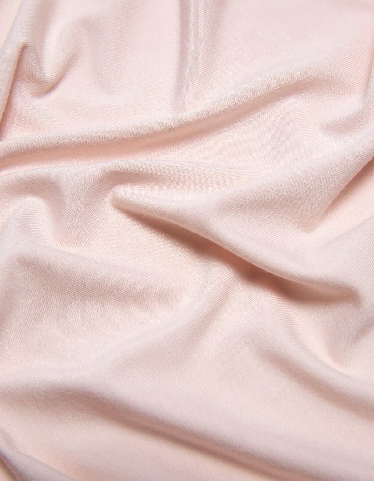 The Bamboo Jersey Sheet Set by Cozy Earth features soft, light pink fabric with subtle folds and gentle wrinkles for a smooth, slightly textured look.|Color:Petal