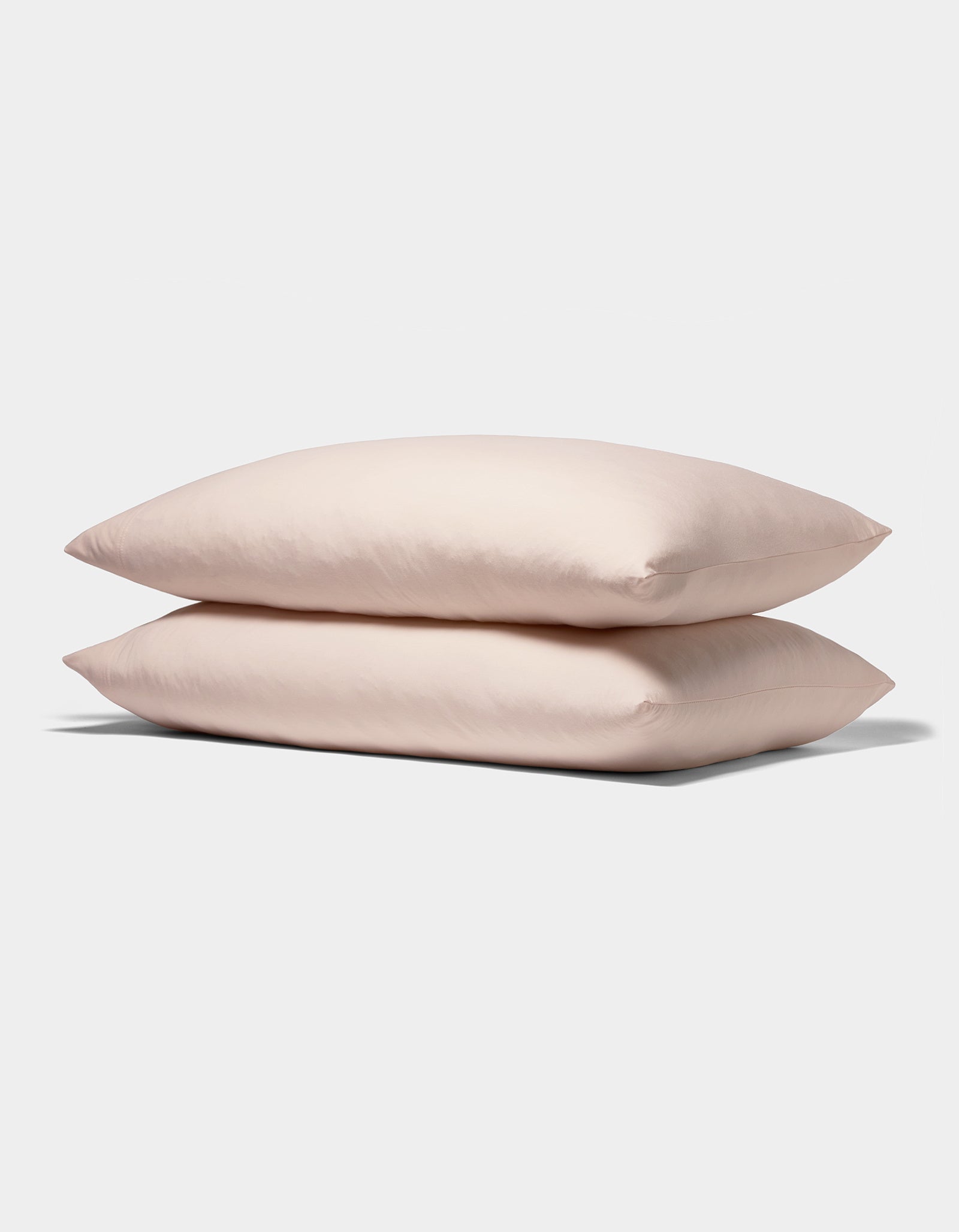 Two Bamboo Jersey Pillowcases from Cozy Earth, in soft light pink, are stacked neatly against a plain white background.|Color:Petal