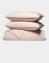 The Cozy Earth Bamboo Jersey Quilt Bundle features two light pink quilted pillows stacked atop a matching quilted blanket, all neatly arranged against a plain white background.|Color:Petal