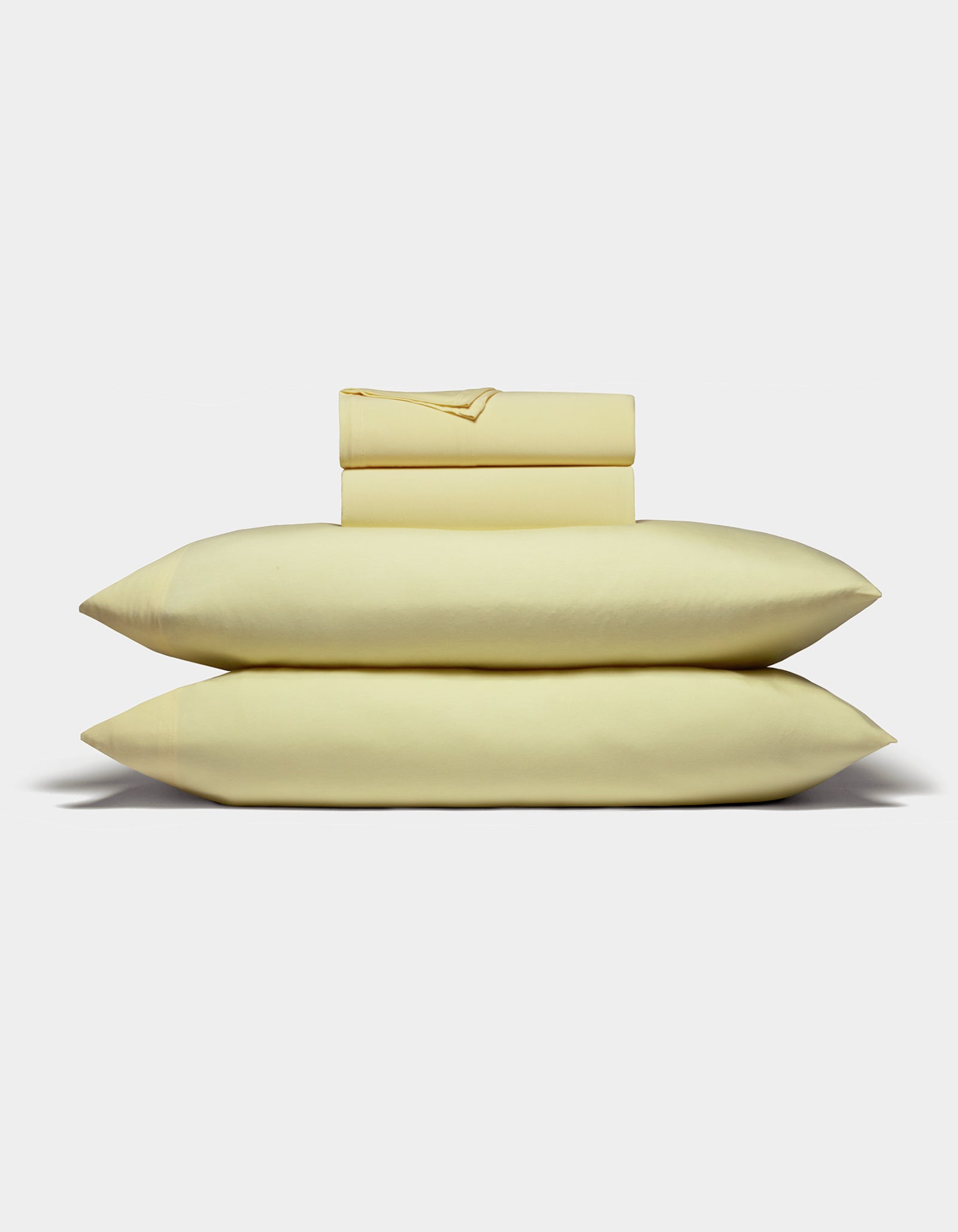 The Cozy Earth Bamboo Jersey Sheet Set is displayed neatly folded with two stacked pillows, a flat sheet, and a fitted sheet in light yellow against a plain white background.|Color:Meringue