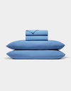 The Cozy Earth Bamboo Jersey Sheet Set, featuring two pillowcases, a fitted sheet, and a flat sheet in blue, is neatly folded and stacked against a plain white background.|Color:Sailor