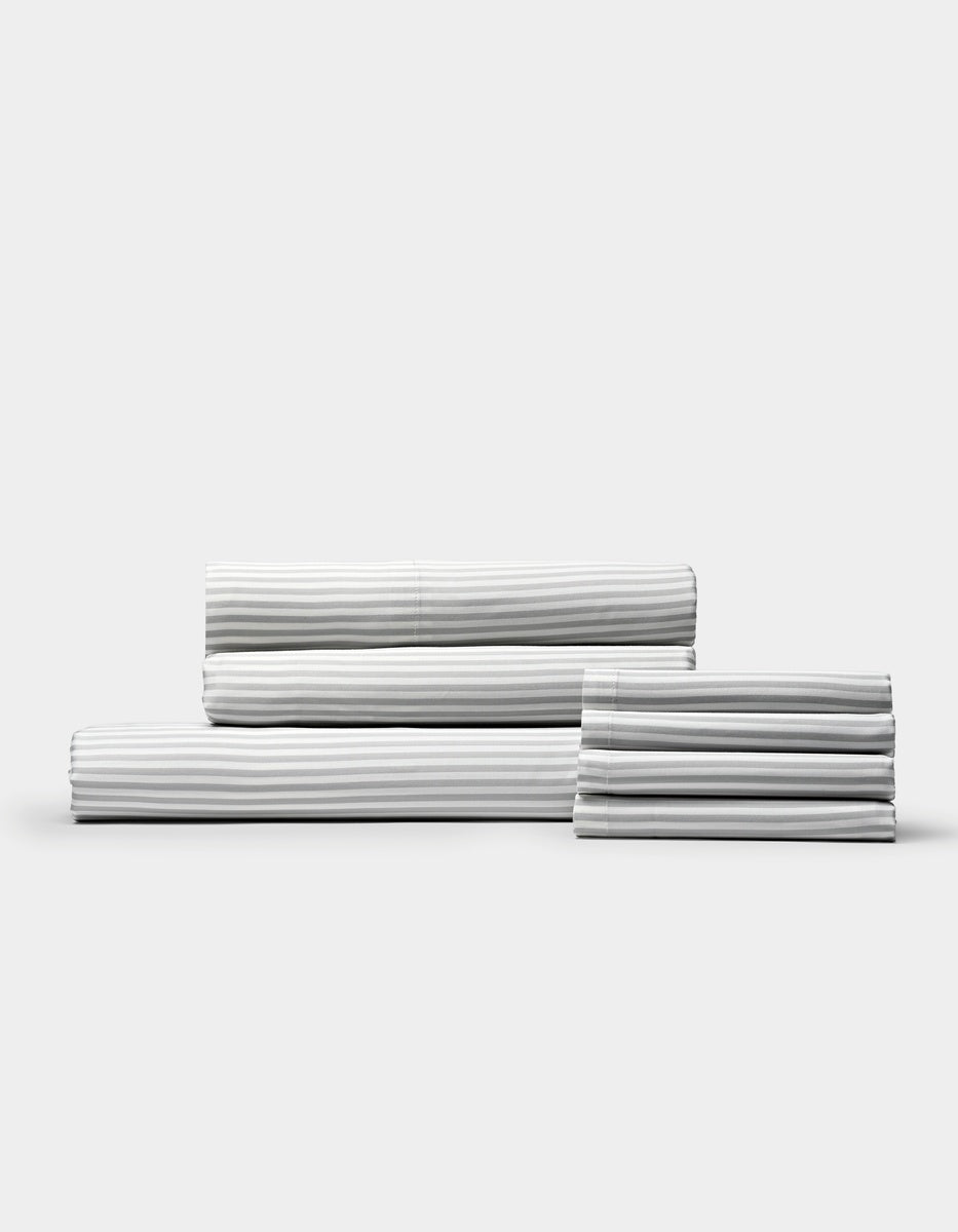 A neatly stacked set of Cozy Earth Bamboo Bedding Core Bundle sheets, featuring white fabric with thin grey stripes, displayed against a plain light background.|Color:Classic Stripe in Dew