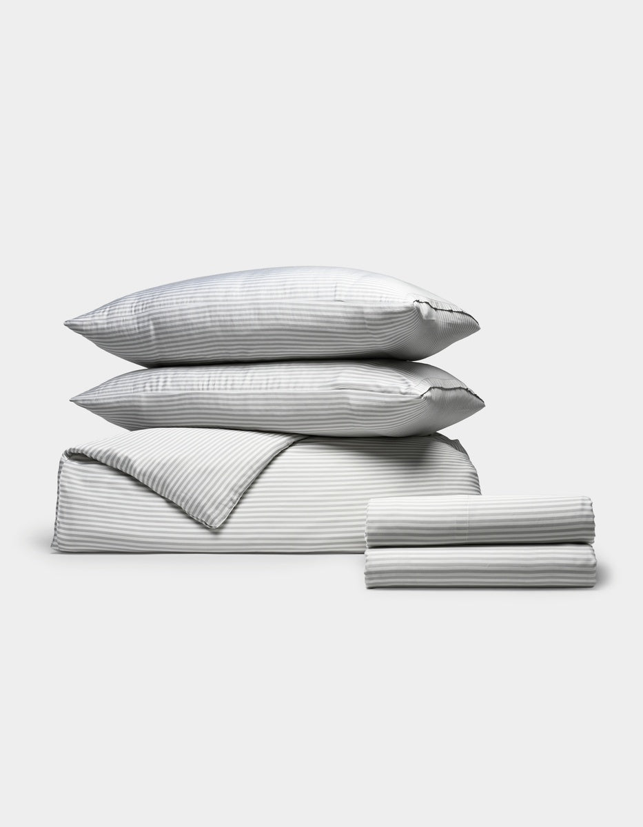 The Cozy Earth Bamboo Bedding Deluxe Bundle, in grey stripes, includes two pillows, a duvet, and sheets neatly folded and displayed on a plain white background.|Color:Classic Stripe in Dew