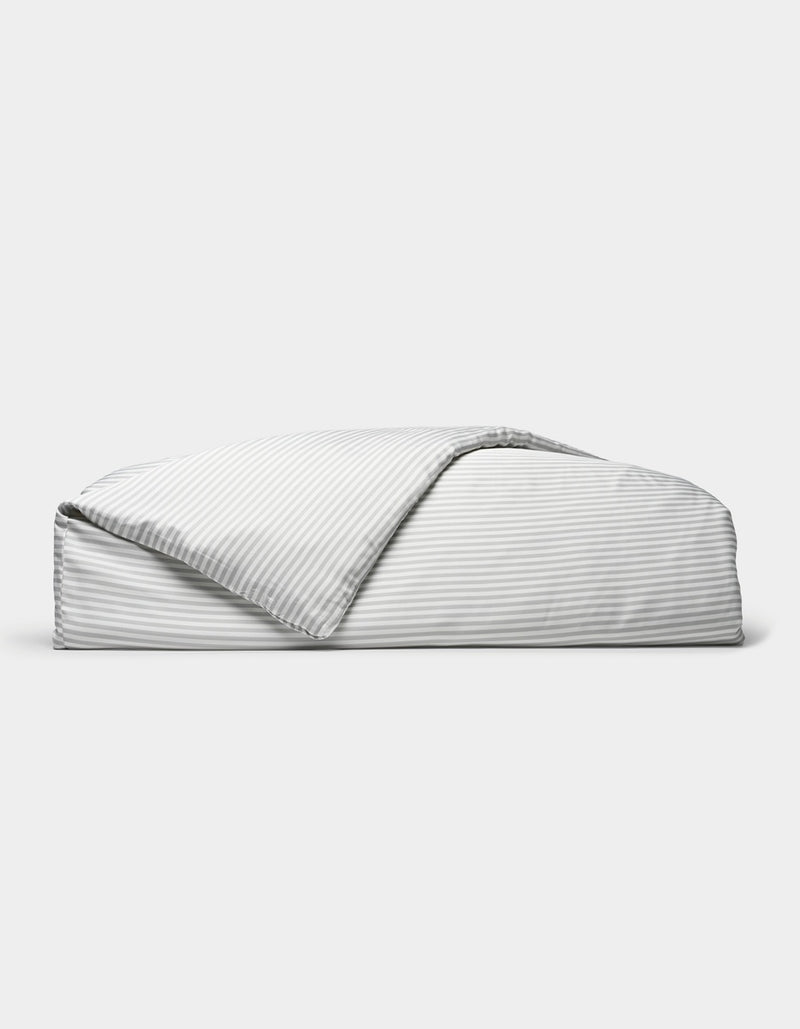A neatly folded Bamboo Duvet Cover by Cozy Earth, featuring light gray and white stripes with one corner flipped open, is displayed against a plain white background.