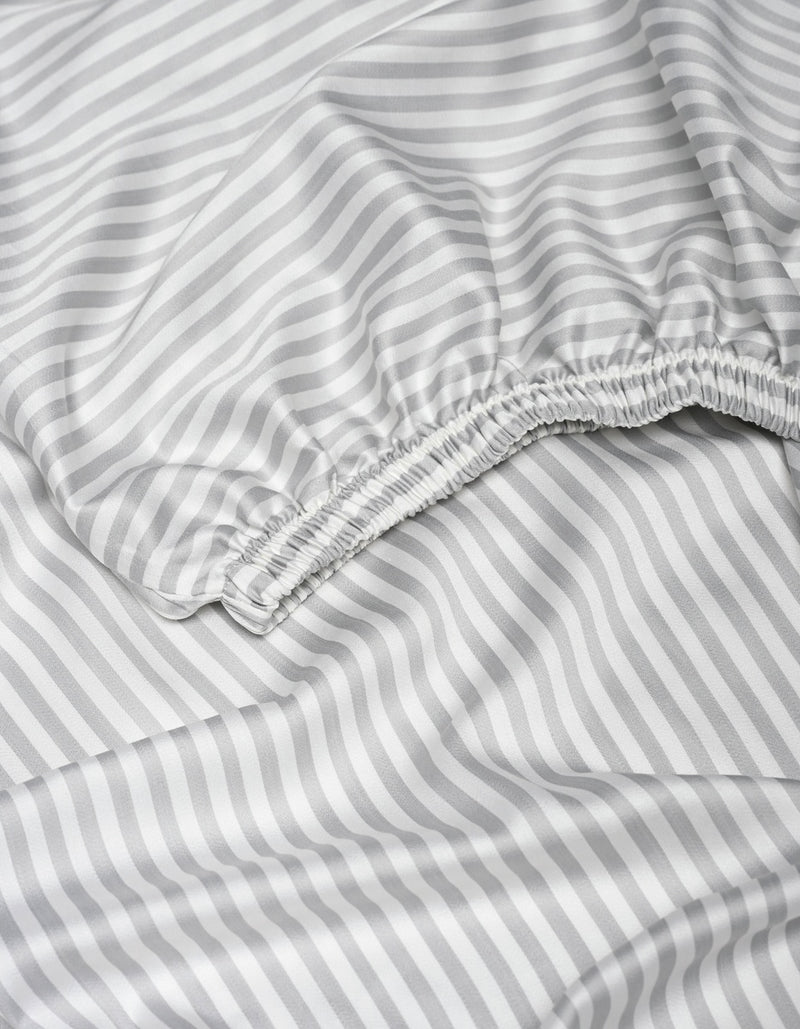 A close-up of the Cozy Earth Bamboo Fitted Sheet displays its gray and white diagonal stripes, featuring a gathered elastic edge and smooth, slightly wrinkled fabric.